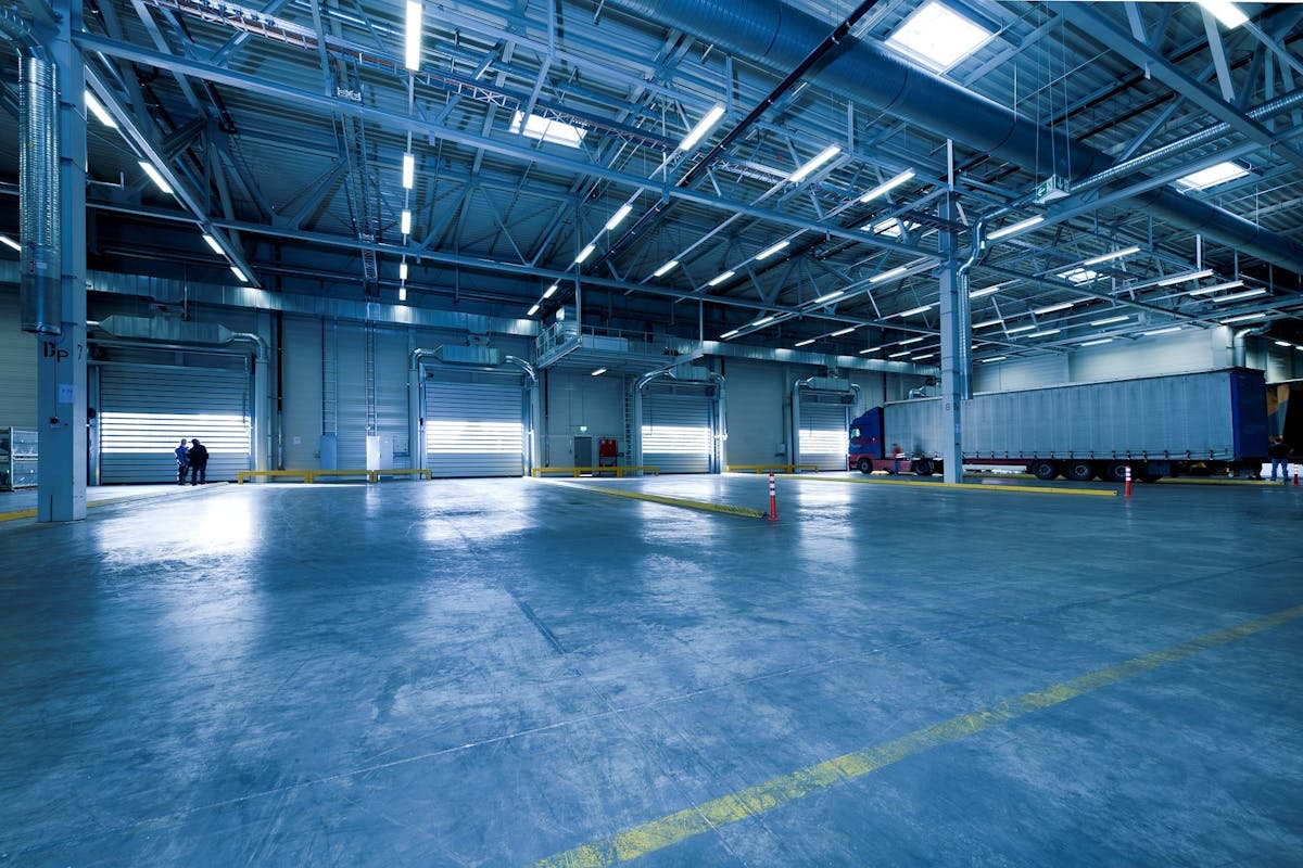 Weite Industriehalle mit poliertem Beton-Boden, gelben Bodenmarkierungen und LKW-Verladung — Beispielbild Industrie-Reinigung.