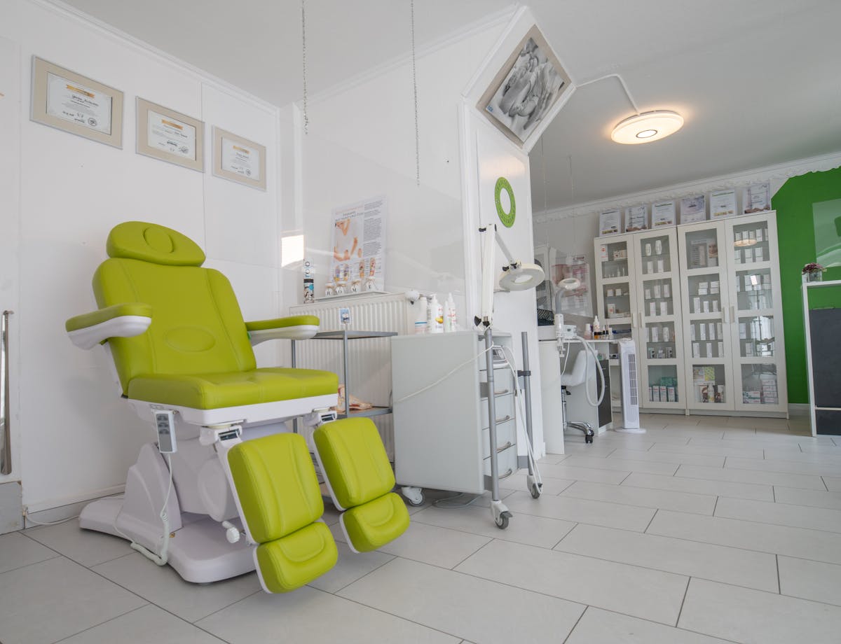Heller Behandlungsraum mit Behandlungsstuhl, Hygiene-Vitrinen und gefliestem Boden — Beispielbild Praxis-Reinigung.